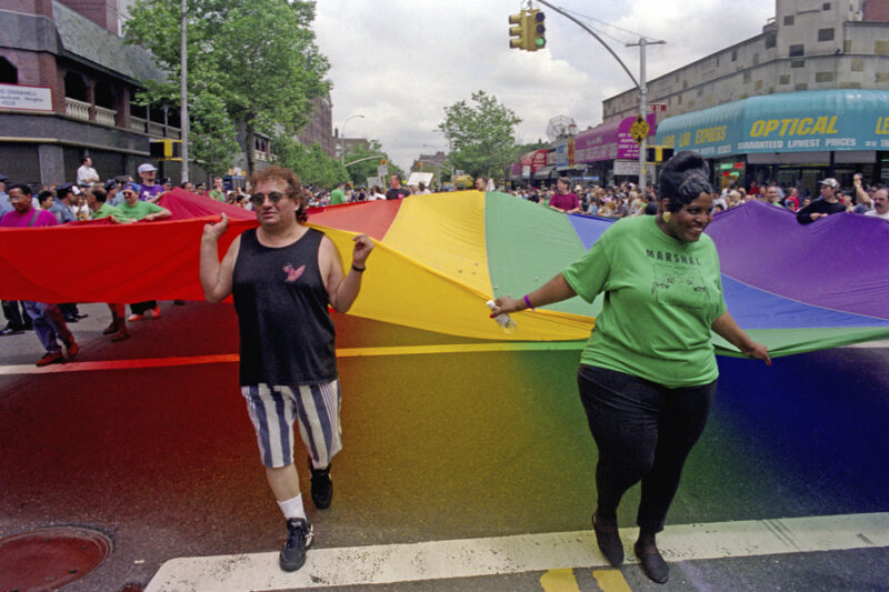Photo of Queens Pride Parade participants carry the LGBT rainbow flag.
