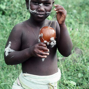thumbnail of A child with white markings on his face while holding an object in his hand.
