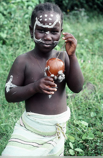 thumbnail of A child with white markings on his face while holding an object in his hand.