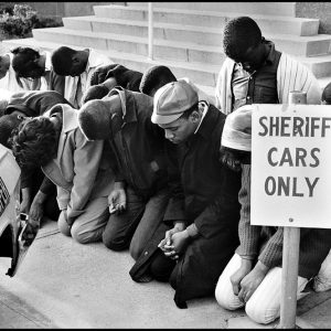 thumbnail of Students praying for jailed voting rights Activist, Dallas County courthouse by Dan Budnik. medium: silver gelatin print. date: March, 1965. dimensions: 13.25 x 11.75 inches